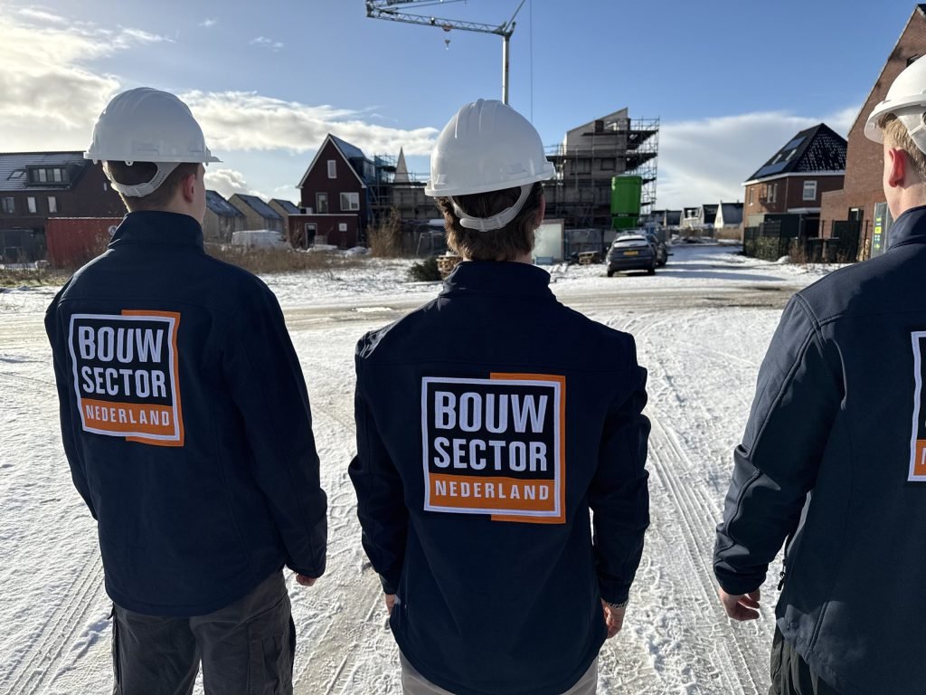 Drie mannen in werkkleding met het logo van Bouwsector Nederland op de rug voor een rij huizen in aanbouw